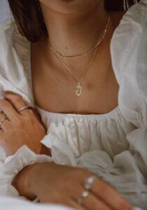 Girl wearing layerd dainty necklace, rings and bracelet in the blog post of 9 Must Have Jewelry For Everyday Wear